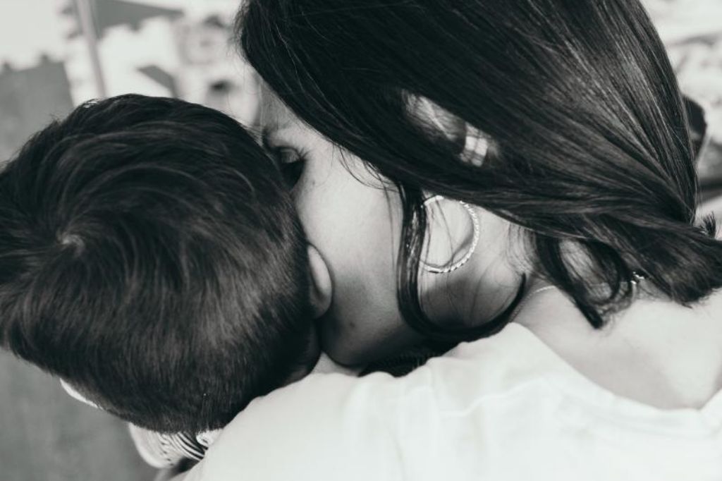 Kaya hugging her son Luca closely, seen from behind in black and white.