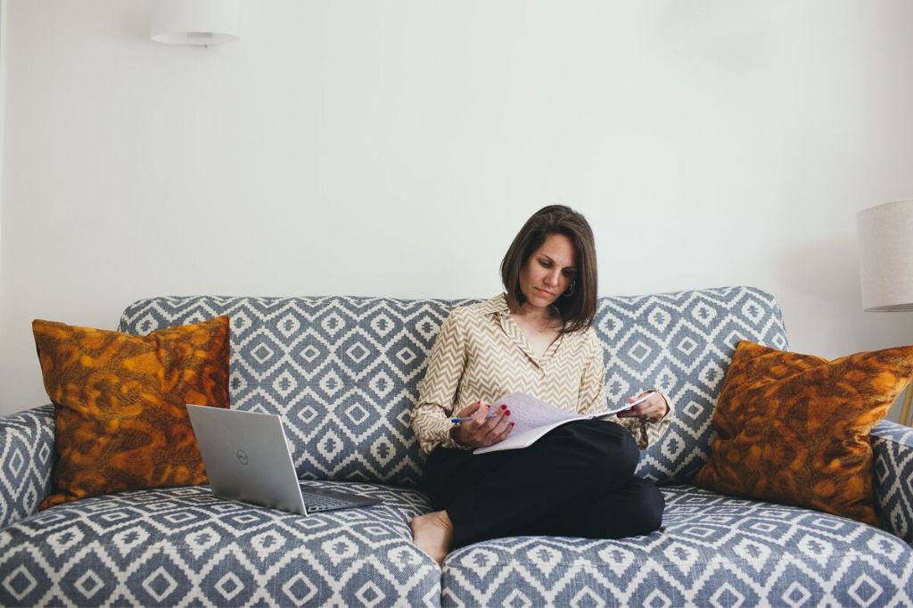 Kaya Ramjee sitting on a patterned sofa reading notes with a laptop beside her.
