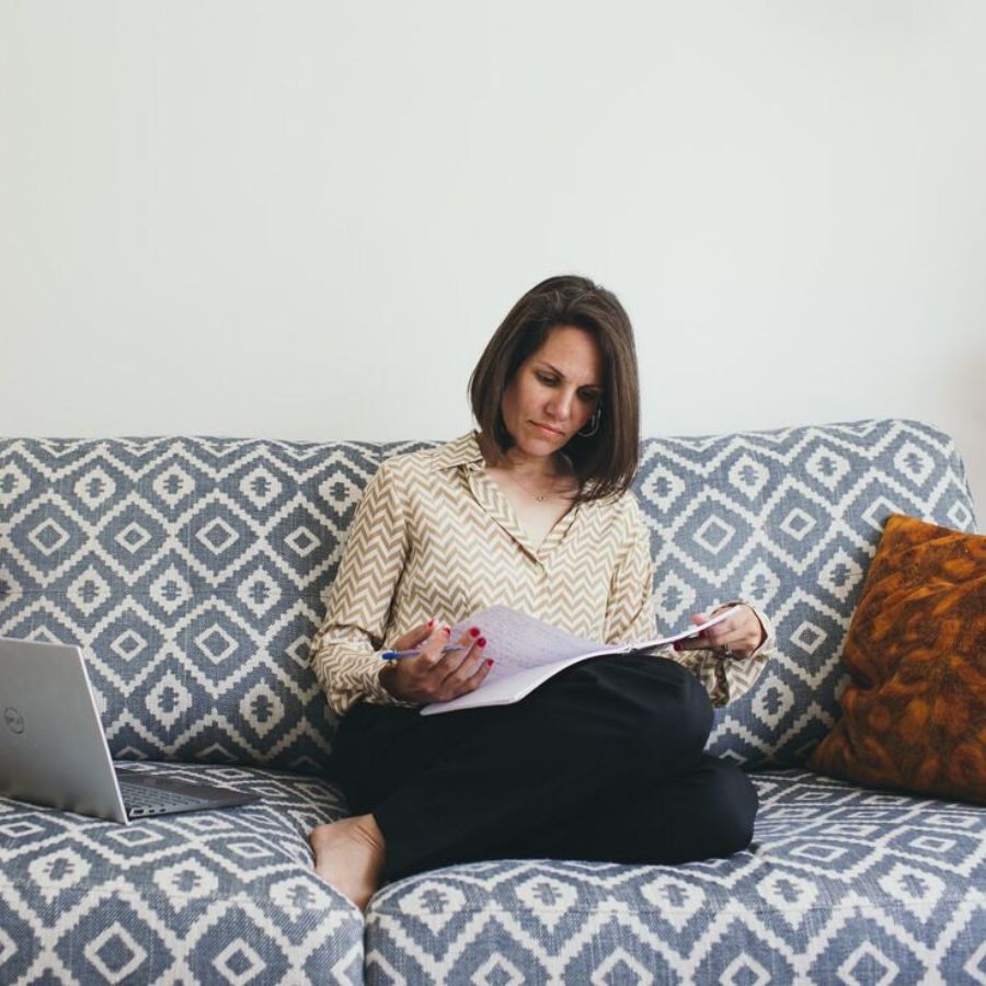 Kaya Ramjee Executive mental fitness coach, sat on patterned sofa reading with laptop by her side
